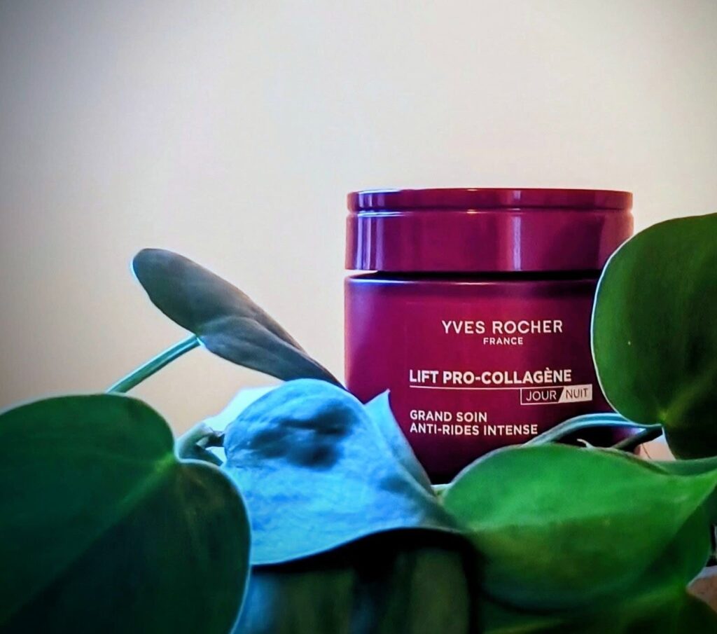 A red jar of facial day cream is hinted behind some stretchy leaves. 