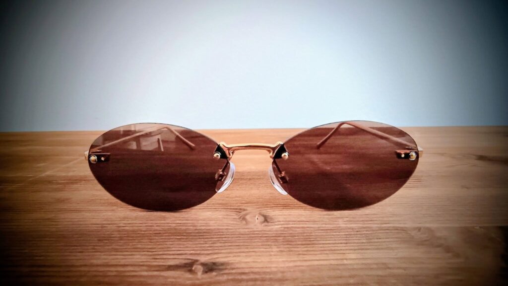 A pair of rimless sunglasses made of a brown shade is laying on a wooden surface